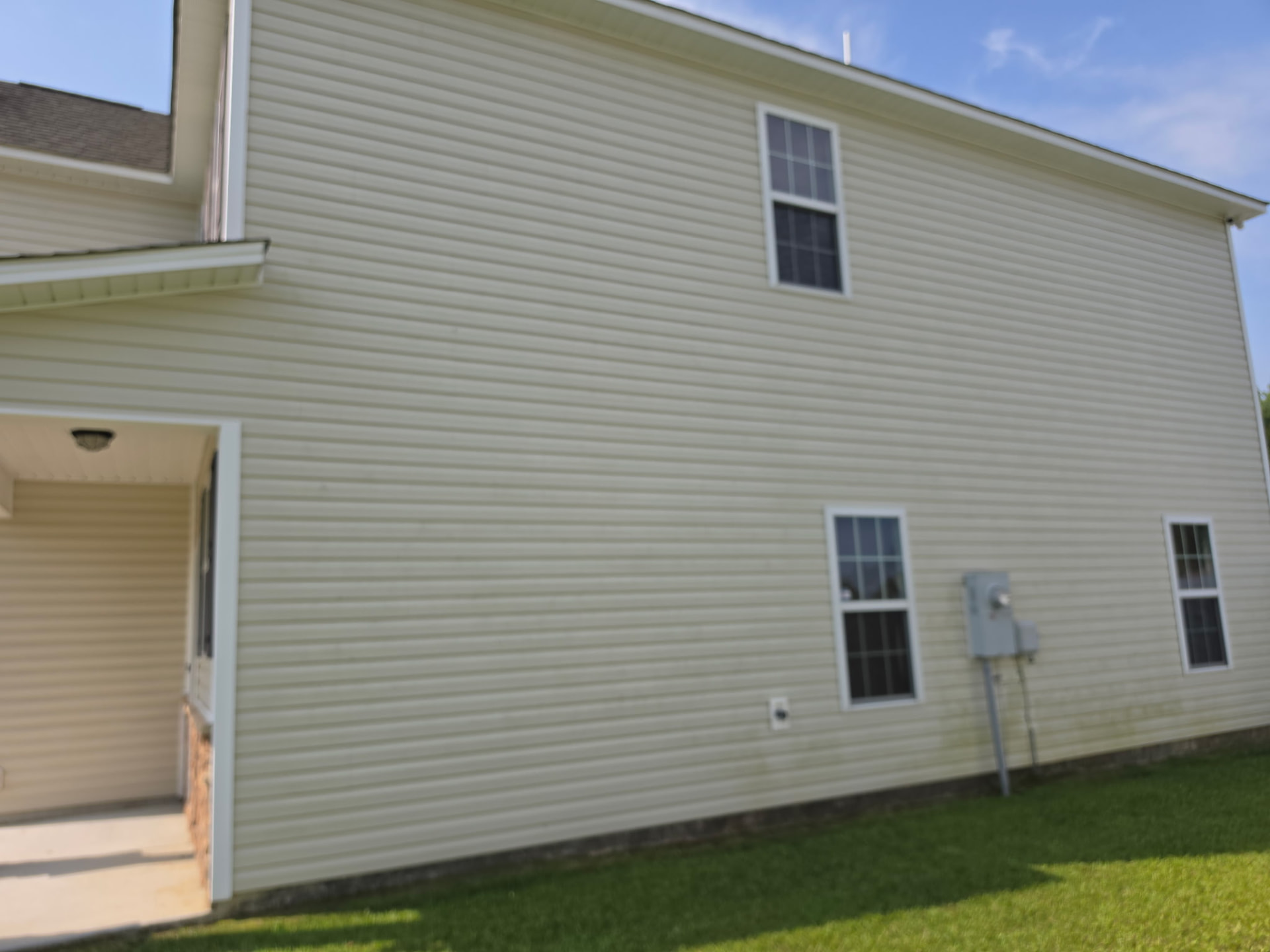 House washing before and after in Jacksonville, NC: heavy green algae on a shaded beige siding wall